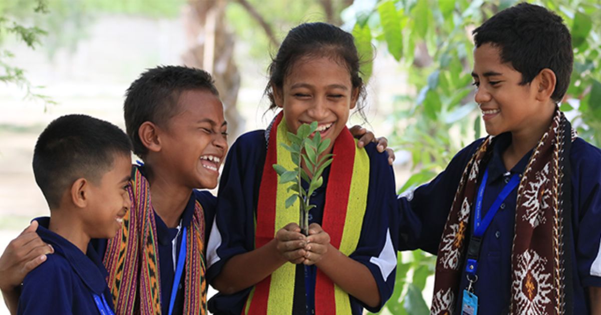A group of four laughing children working in a veggie garden
