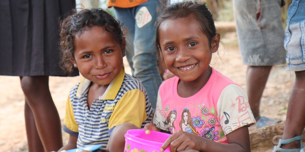 Two young smiling children eating their rice meal prepared by Cristina