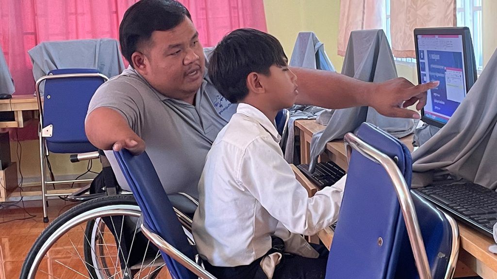 Longkut teaching a young student on a computer