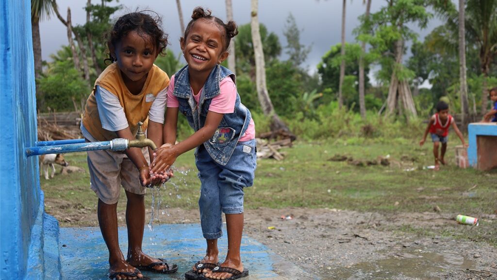 Two young children enjoying fresh water form a newly installed water tank