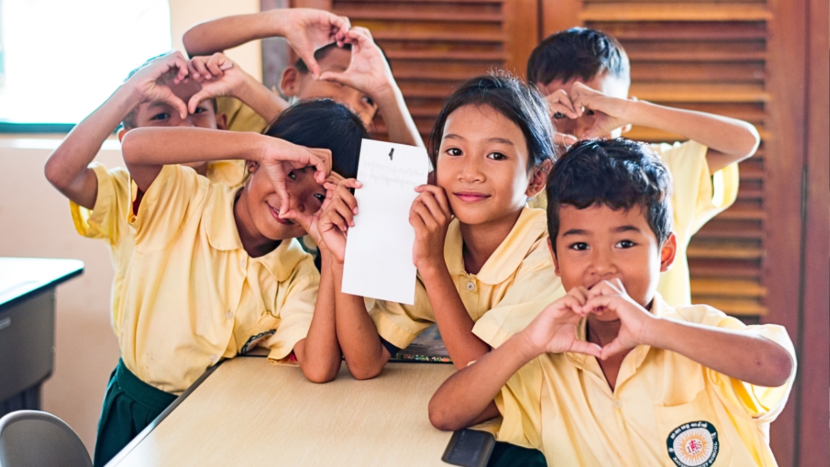 Children in a school in Cambodia making love hearts with their hands