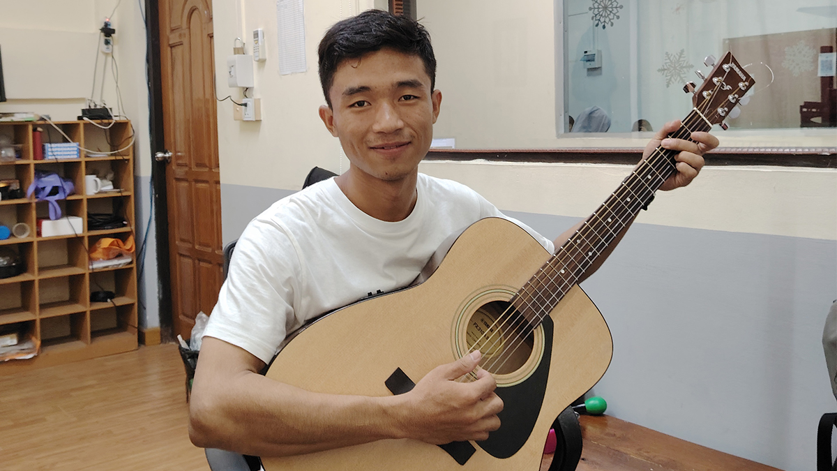Micahel in a schoolroom playing an acoustic guitar