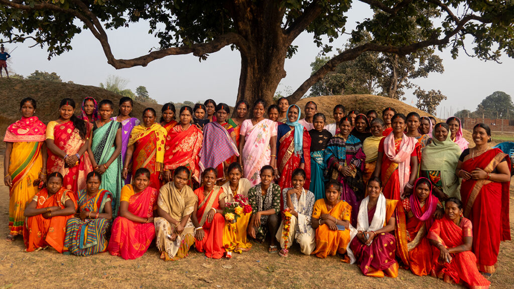 A group of women in bright saris gather under a tree in India