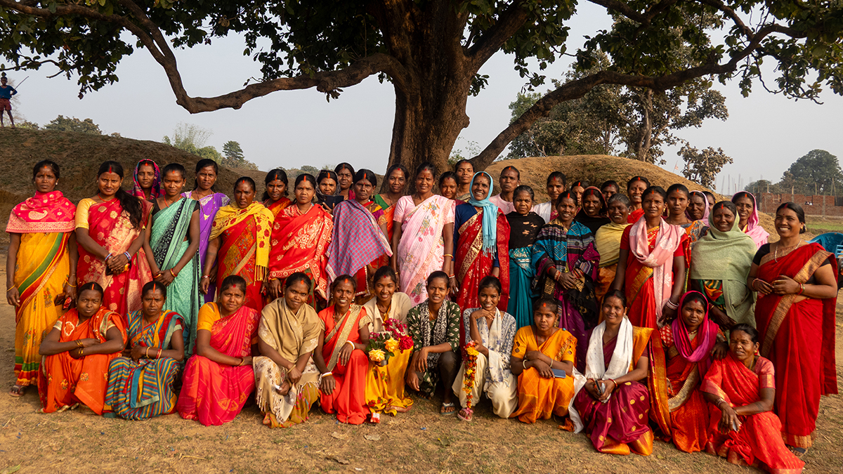 A group of women in bright saris gather under a tree in India