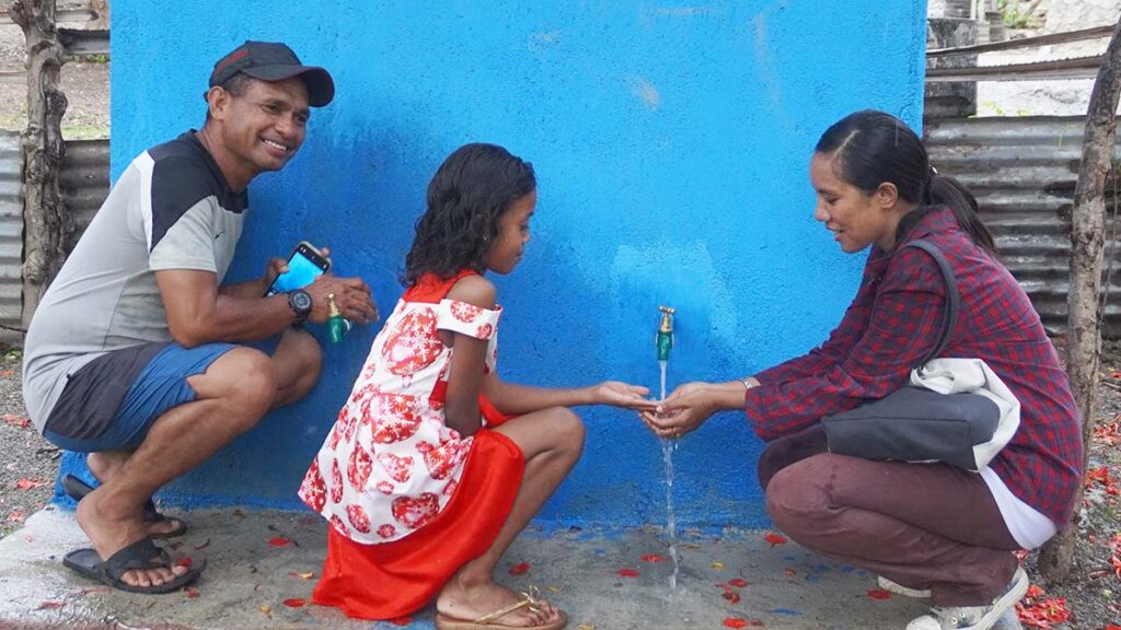 A mother, father and child enjoy clean running water from one of the new water tanks in the village 