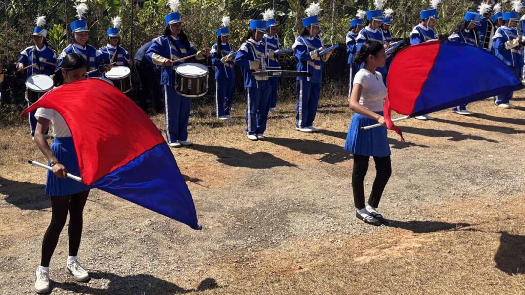 A children's marching band and flag wavers welcome the team at Gonzaga village
